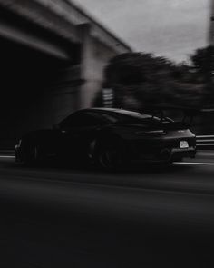 a black sports car driving down the road in front of an overpass and bridge