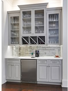 a kitchen with gray cabinets and white counter tops is pictured in this image, there are wine glasses on the glass cabinet doors