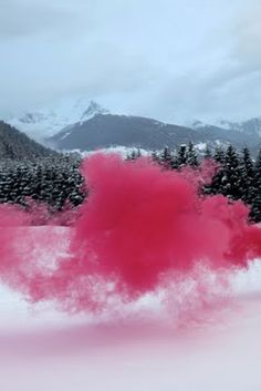 pink powder is spewing out into the air in front of trees and mountains