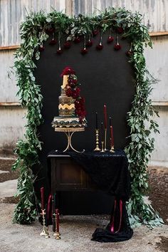 a wedding cake on top of a table with candles and greenery around the edges