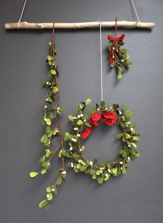 two wreaths hanging from a wooden stick with red bows and green leaves on them