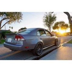 a car is parked on the side of the road in front of some trees at sunset