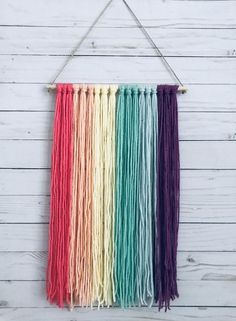 a multicolored wall hanging on the side of a white wooden wall with string attached to it