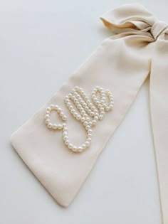 a white tie with pearls on it and a monogrammed letter in the middle