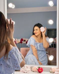 a woman sitting in front of a mirror holding a pink flower up to her face