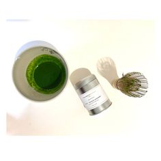 a cup of green tea next to a whisk and some herbs on a white table