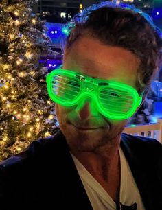 a man wearing neon green glasses in front of a christmas tree with lights on it