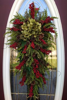 a christmas wreath hanging from the side of a door with red berries and greenery