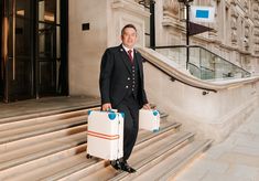 a man in a suit and tie holding two suitcases on the steps of a building