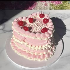 a pink and white cake with cherries on top sitting on a marble countertop