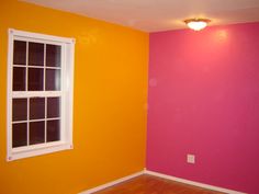 an empty room painted bright pink and orange with a window on the far wall in front of it