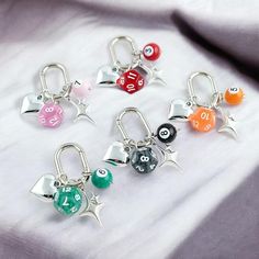 six different colored dice charms with numbers on them sitting on a white cloth covered surface