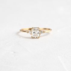 an engagement ring with three stones on the band and a diamond in the middle, sitting on a white surface