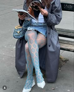 a woman is sitting on a bench reading a book and wearing fishnet tights