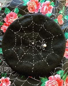 a black hat with spider webs on it and flowers in the background, sitting on a table cloth