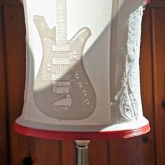 a lamp shade with a guitar on it's side and red trim around the edge