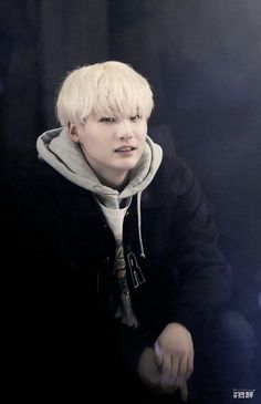 a young man with blonde hair wearing a black hoodie and looking at the camera