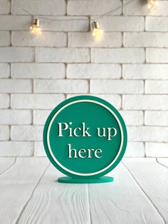 a sign that says pick up here on a white table with lights in the background