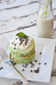 a stack of green pancakes with whipped cream and chocolate chips on top next to a glass of milk