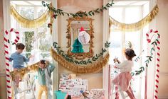 two children standing on ladders in front of christmas decorations and gifts under a window