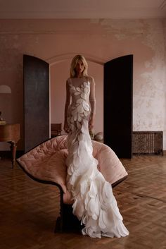 a woman in a white dress standing on a pink couch with her back to the camera