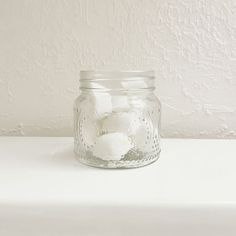 a glass jar filled with white flowers on top of a table next to a wall