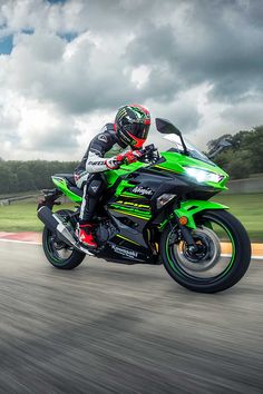 a man riding on the back of a green motorcycle down a race track with trees in the background