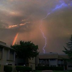 a rainbow appears in the sky as a lightning strikes behind some apartment buildings on a cloudy day