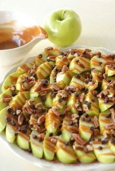 a white plate topped with sliced apples covered in caramel and pecans next to an apple