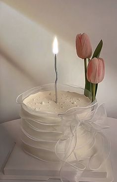 a white cake with pink flowers on top and a single candle in the middle that is lit