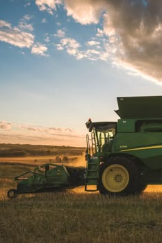 a large green truck parked on top of a grass covered field next to a tractor