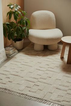 a living room with a chair, ottoman and potted plant on the floor in front of it