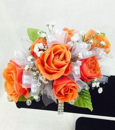 an orange and white corsage bouquet on a black box with pearls, ribbons, and flowers