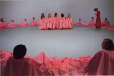 a group of women in pink dresses sitting on top of a circular surface with people standing around