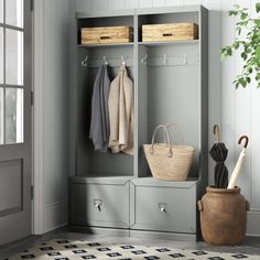 a white coat rack with baskets, umbrellas and coats hanging on the wall next to it