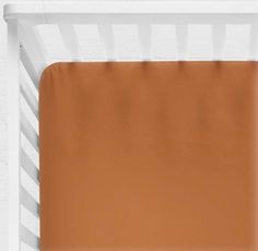 a baby crib with an orange sheet and brown sheets on the bottom half, in front of a white brick wall