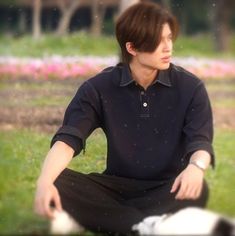 a young man sitting on the ground with his legs crossed in front of him, wearing a black shirt and black pants