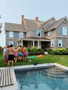 a group of people standing in front of a swimming pool next to a large house