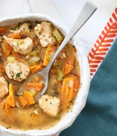 a white bowl filled with chicken and vegetable soup on top of a blue towel next to a spoon