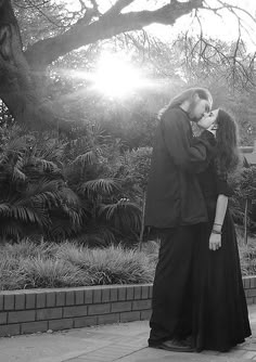 black and white photograph of two people standing in front of a tree with the sun behind them