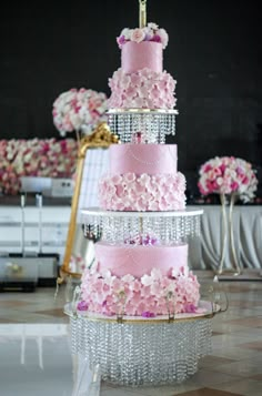 a three tiered cake with pink flowers on the top is surrounded by crystal beading