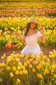 a woman in a white dress and hat sitting in a field of yellow tulips