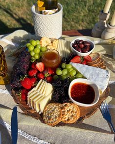 a platter filled with cheese, crackers and fruit sits on a picnic table