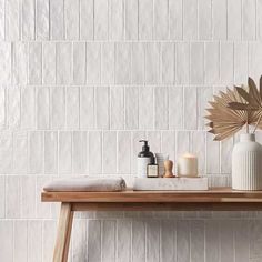 a wooden table topped with two vases filled with candles and other items next to a white tiled wall