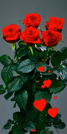 a vase filled with lots of red roses on top of a wooden table next to green leaves