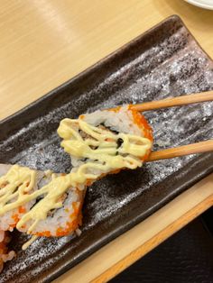 two sushi rolls with sauce and chopsticks on a black plate