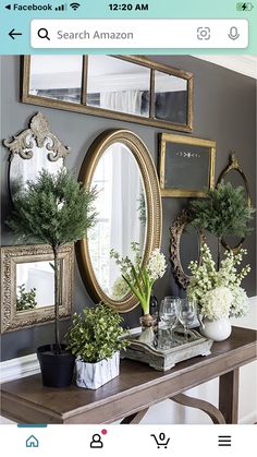 a table topped with mirrors and plants next to a wall filled with framed pictures on it