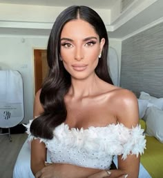 a woman with long dark hair wearing a white feathered dress and posing for the camera