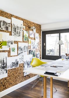 a room with a desk, chair and pictures on the wall behind it in front of a window