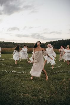 a group of women in white dresses are dancing on the grass